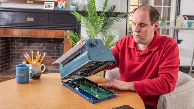 A blind man inserting a Braille Bloom into a Perkins Brailler.